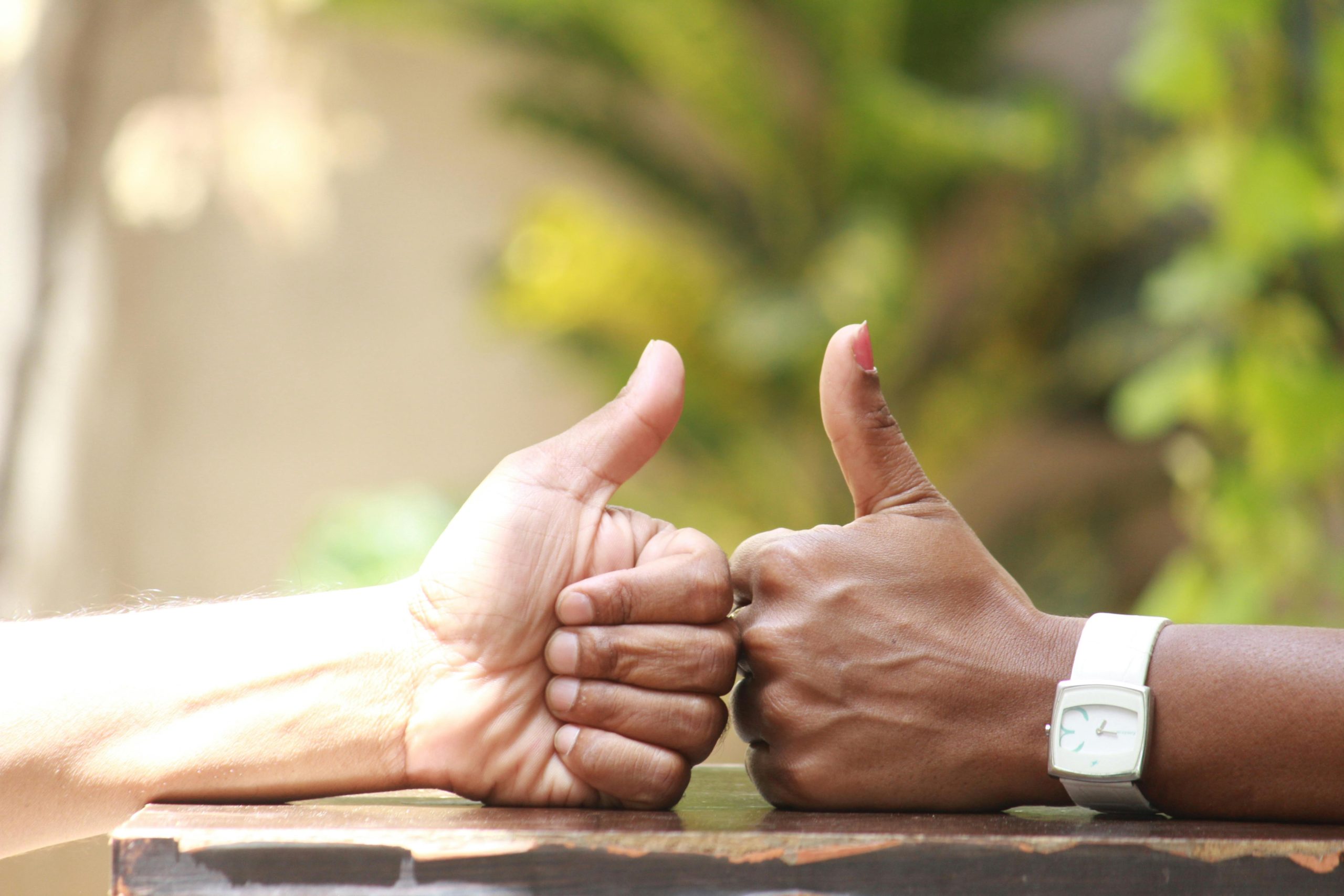 Close-up of two people giving thumbs up outdoors, symbolizing agreement.