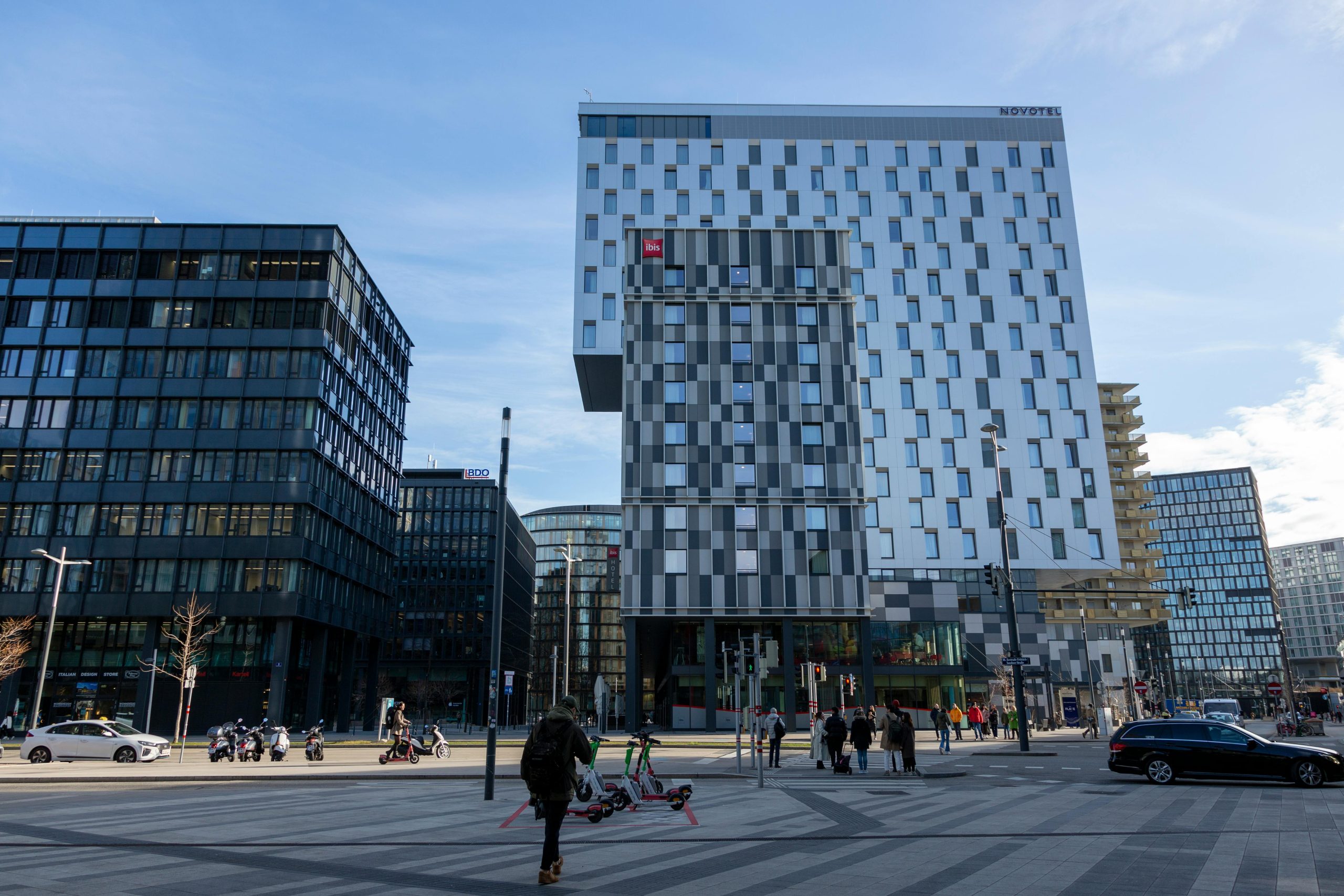 Modern office buildings in a city center with people and traffic activity.